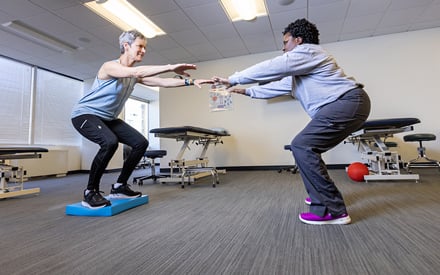 A physical therapist educating a patient on how to perform a strength and balance exercise.